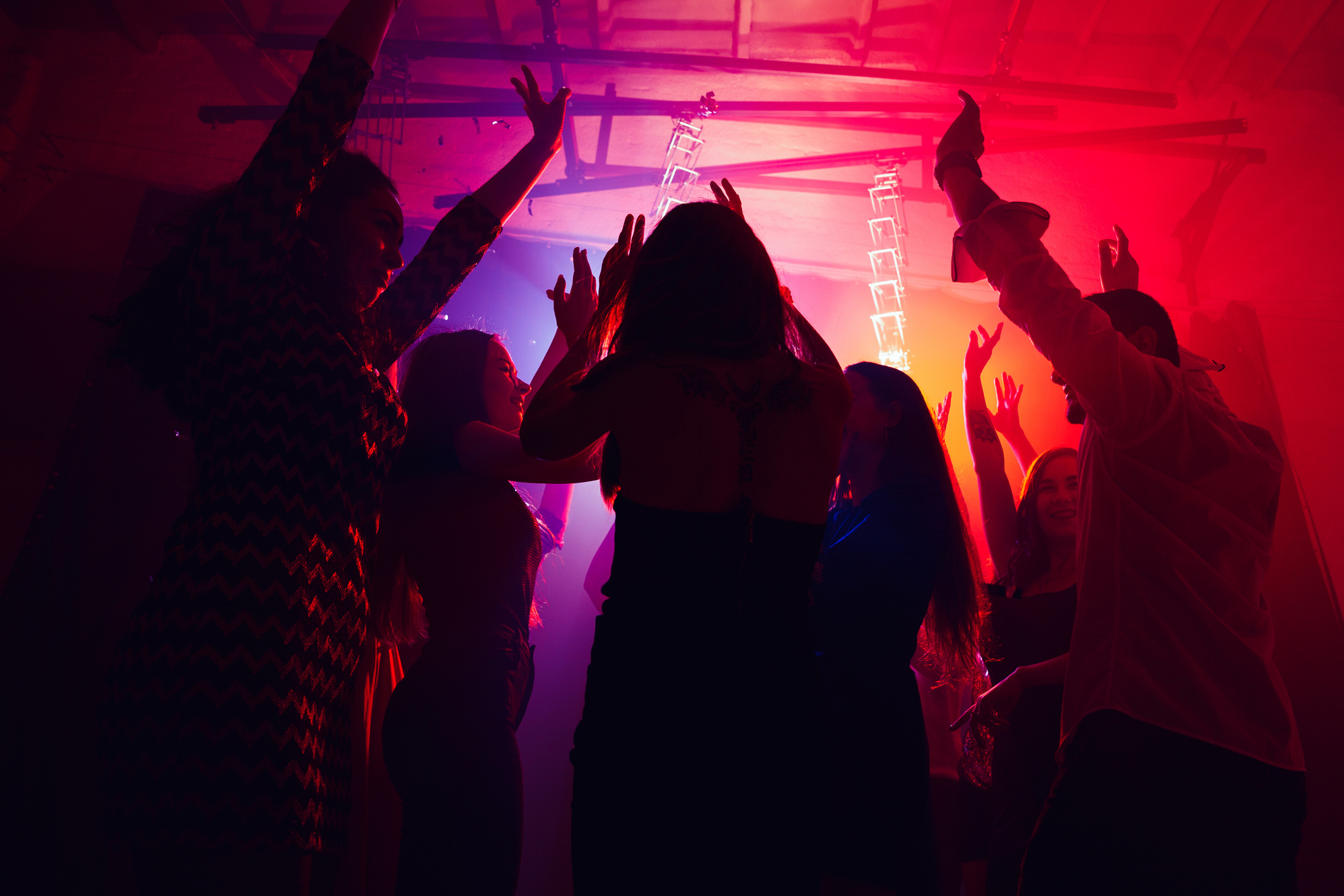 A crowd of people in silhouette raises their hands against colorful neon light on party background